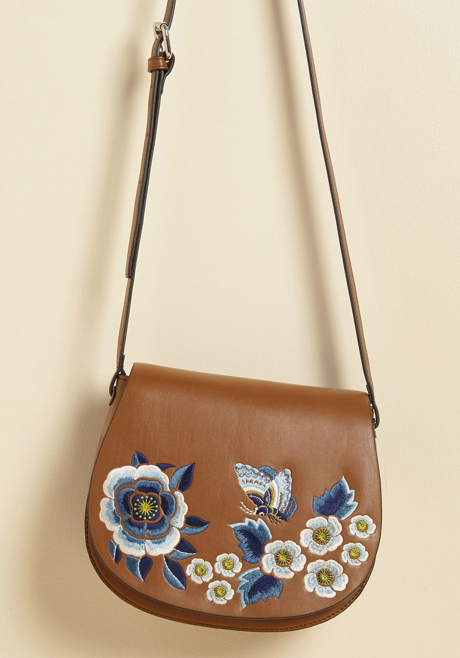  - From brunch dates to boutique hops and beyond, there isn't a scenario out there that wouldn't welcome this tan satchel! The rounded silhouette of this faux-leather shoulder bag is host to a cool-toned collection of embroidered blooms and butterflies - det