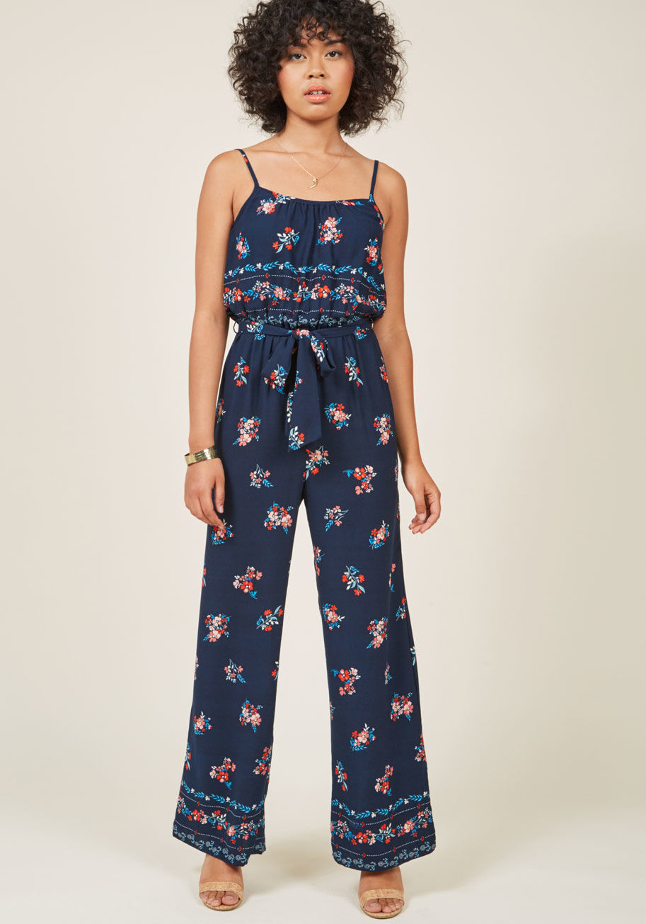  - With its sleek straps, flattering gathered waist, and Americana floral print, this navy jumpsuit ensures you'll feel your boldest and best with every wear! But, the fun doesn't end there - a matching sash, wide legs, and a gorgeous border print 'round the