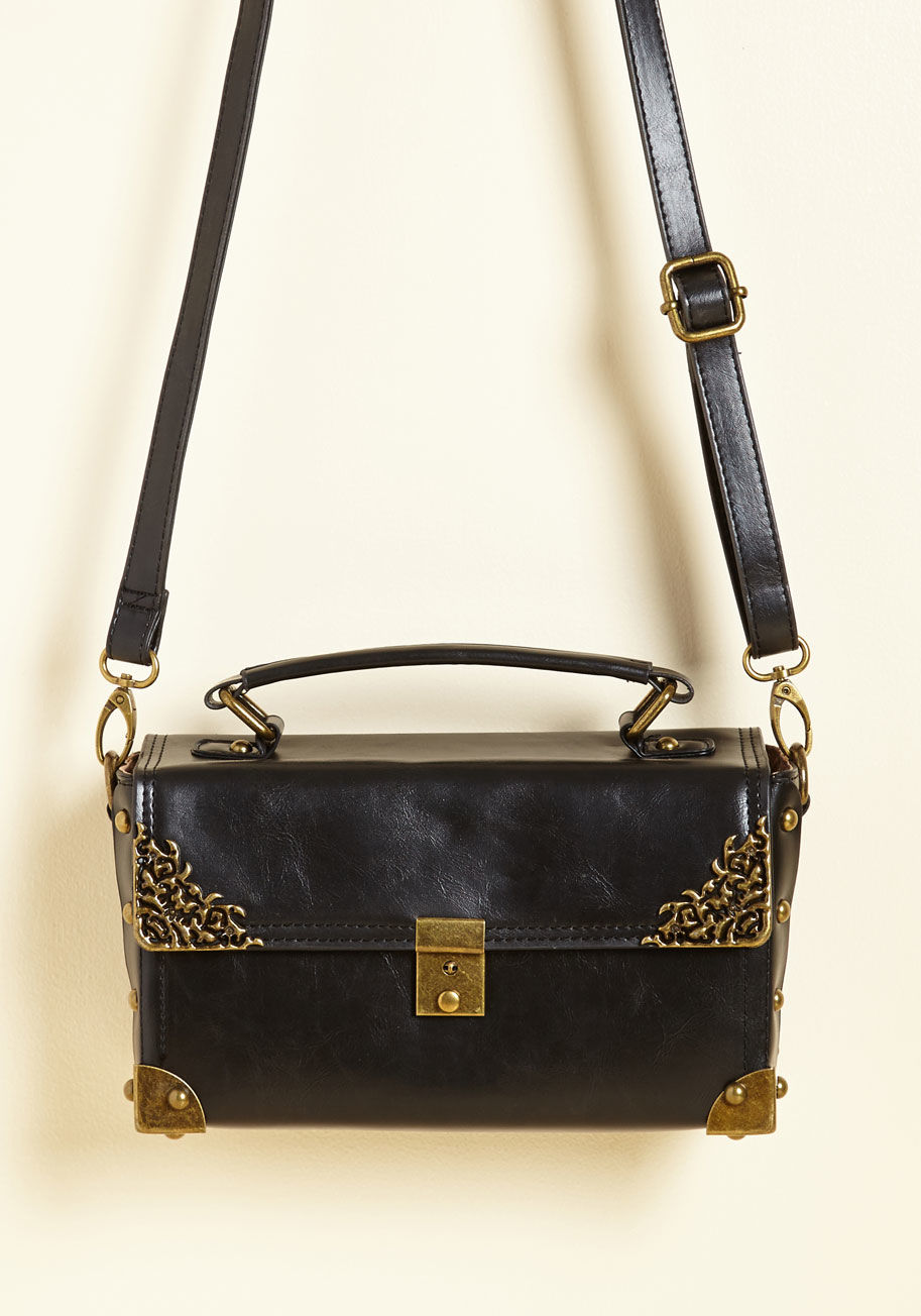  - Your day of memory making with this black crossbody bag concludes with plans to continue tomorrow! The brassy accents atop the vegan faux leather - paired with a cool closure that opens by sliding its button down and a pocketed interior - are like photo c