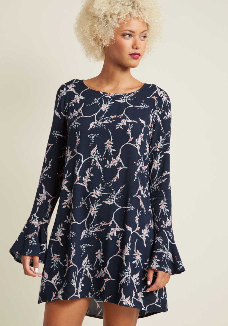 13157701 - Deciding to don this navy blue shift dress can only ever end well! Its sweet long sleeves form into flared cuffs that flutter alongside its loose silhouette, while its elegant blossoming branch print takes on the loveliest rose, rust, and white tones. Sli