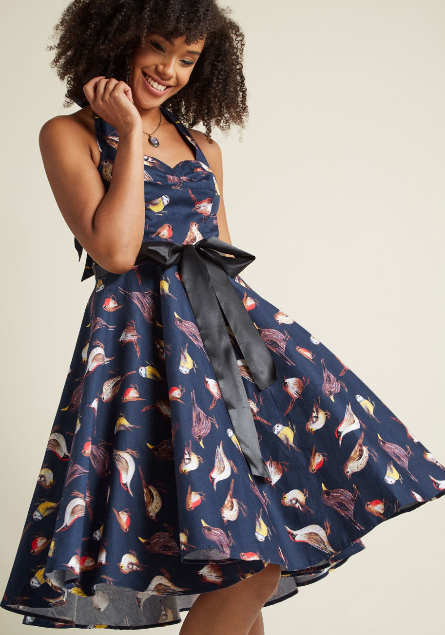 17346 - Giving your look a retro refresh is made simple with the addition of this navy blue sundress to your wardrobe! Halter ties emphasize the sweetheart neckline and flattering princess seams of this mid-length marvel, as its black satin bow and pretty bird pr