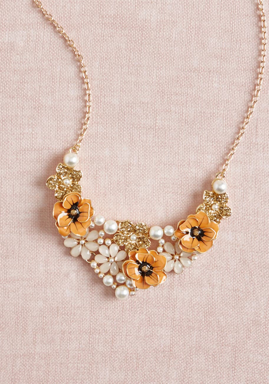 461257N-001 - Swoon for the sparkles, gush over the gloss, and buzz about the beads of this floral statement necklace! Pearl-inspired accents, glimmering rhinestones, faceted blush petals, and sleek orange blossoms culminate atop the gold base of this elegant accessory