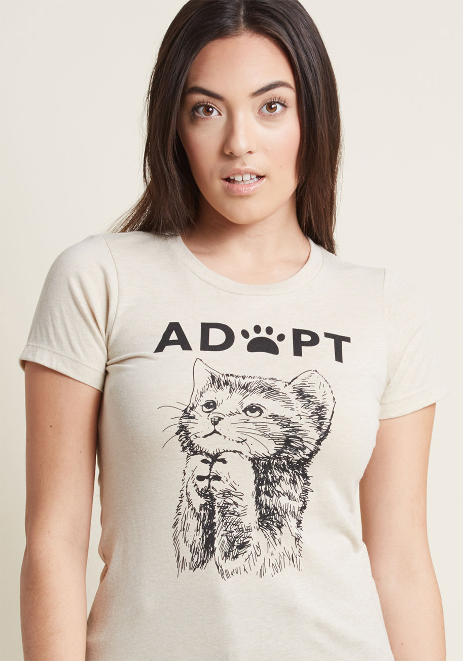 ADOPT TEE - Show your rescued fur baby just how much they mean to you by sporting this graphic tee for cuddle time! This oat-hued T-shirt features a darling tabby screen print along with a 'paws-itive' message, reminding the world of all the sweet pets out there look