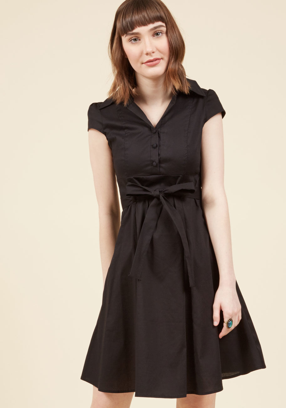 D-1530-1-blk - In this &lsquo;50s-inspired shirtdress, your date at the ice cream parlor is a stylish one! The deep black hue, fabric-covered buttons, and slight stretch to the cotton blend of this eye-catching dress make it a cute wear