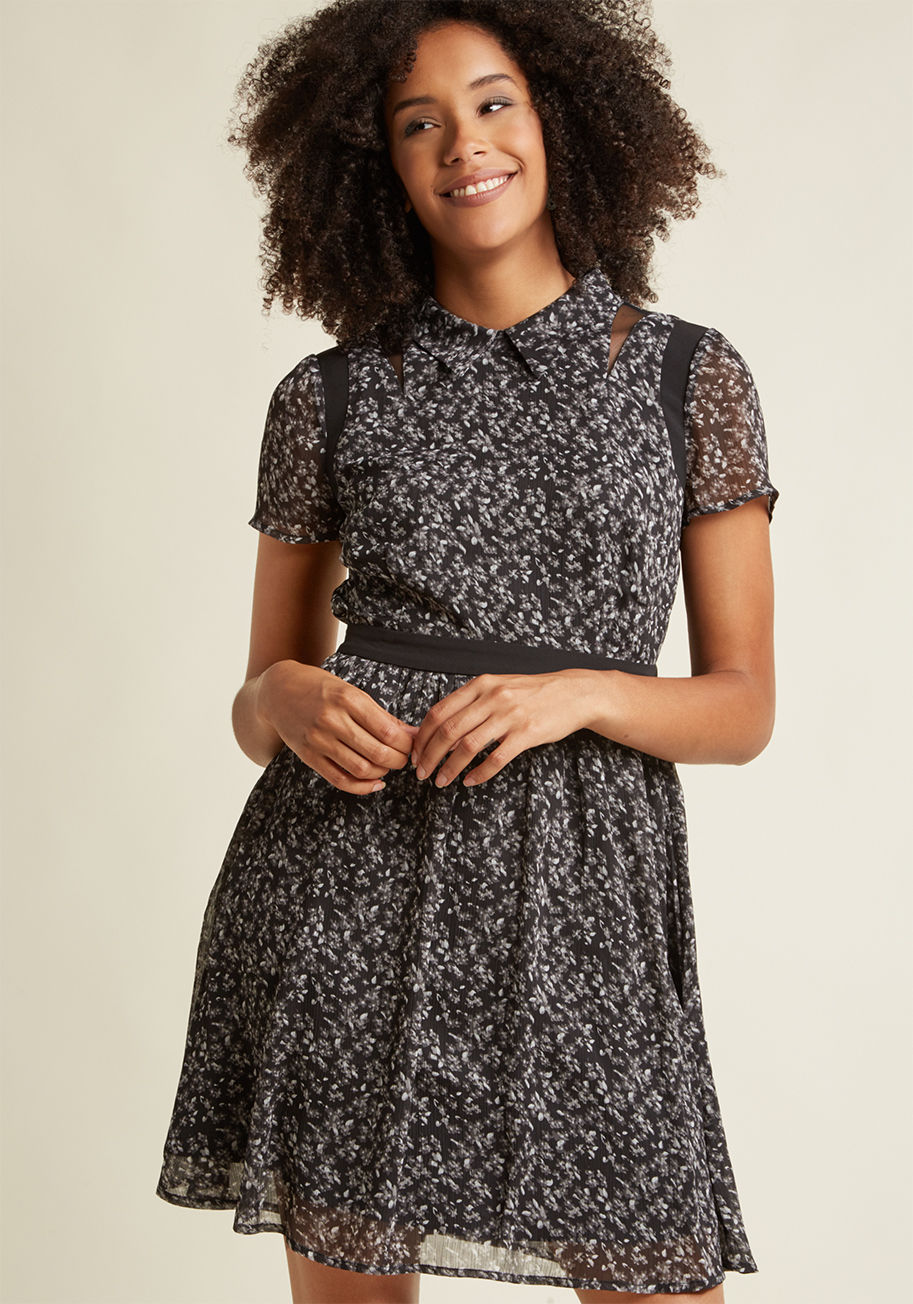 D9797 - This black A-line dress introduces element of femininity, edge, and sophistication into your look all at once! It's the unique combo of grey wildflowers, black mesh shoulder accents, and a button-free bodice that make this chiffon shirt dress what it is. 