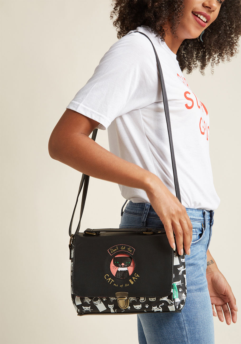 DD SAT CAT - Show off your love for your favorite four-legged friends by prowling around with this black shoulder bag by Disaster Designs! A collection of white kitties romp and play all over the vegan faux-leather exterior of this pink-lined bag, while an especially 