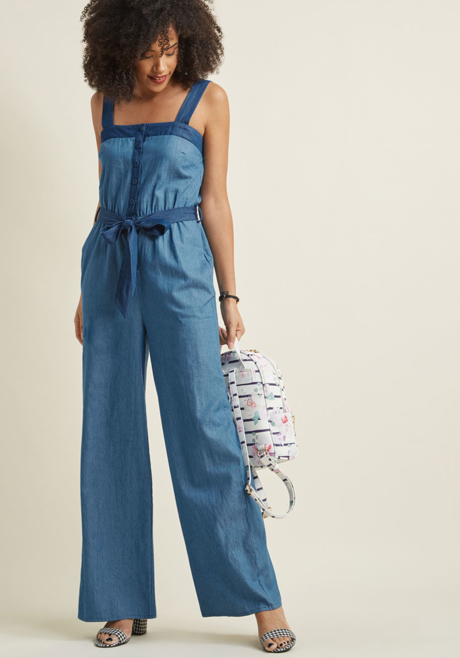 MCB1346 - The versatile design of this chambray jumpsuit welcomes a whole host of accessories, including the greatest one of all - your genuine smile! In addition to a contrast motif at the straps, placket, and self sash, this winning one piece touts handy pockets 