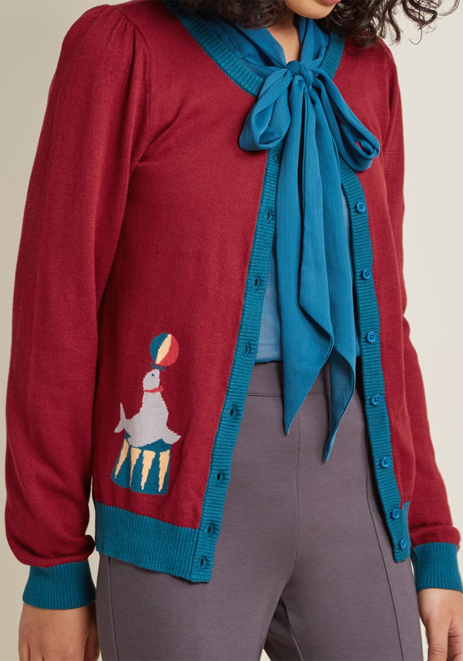 MCS1170 - This burgundy cardigan is just one of many examples of your effortless play between composure and quirk! Part of our ModCloth namesake label, this teal-trimmed layer touts an intarsia seal balancing a beach ball at each hip, expressing the whimsical side 