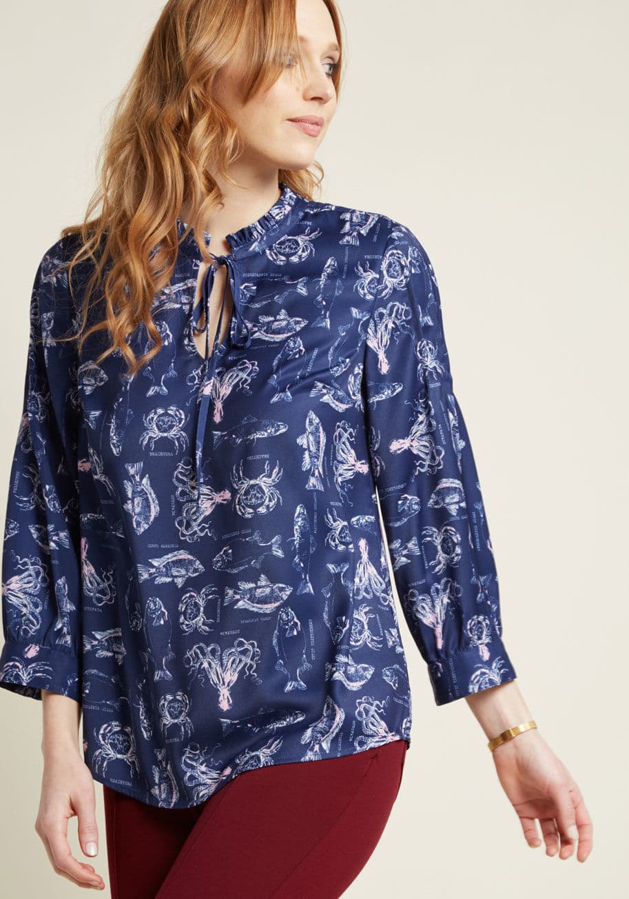 MCT1506 - If unexpected style makes you smile, then this navy blouse from our ModCloth namesake label is guaranteed to make you beam! Ruffles at the tied neckline, pintucks at the shoulders, and cropped enable this silky top to reflect the carefree vibe you hold ne