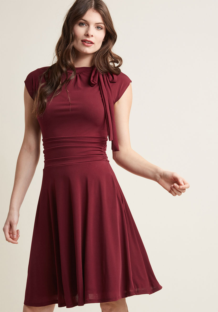 MDD1155 - Jump into this burgundy dress and meet your darling on the dance floor! The bow-topped neckline of this look bounces with your every tango step, while the ruched details hug your waist as you flash your footwork. With a retro-infused shape, this pretty pi