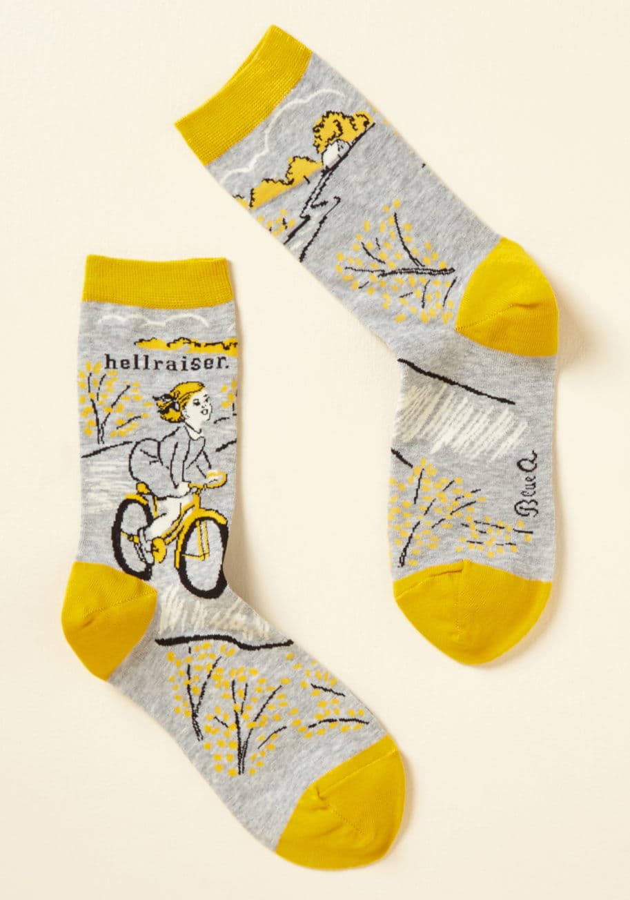 SW422 - Have you ever considered that underneath every poised ensemble is a real troublemaker? These grey crew socks - touting bright yellow trim and a mischievous blondie riding her bike - uphold the notion that hellions are the most haute!