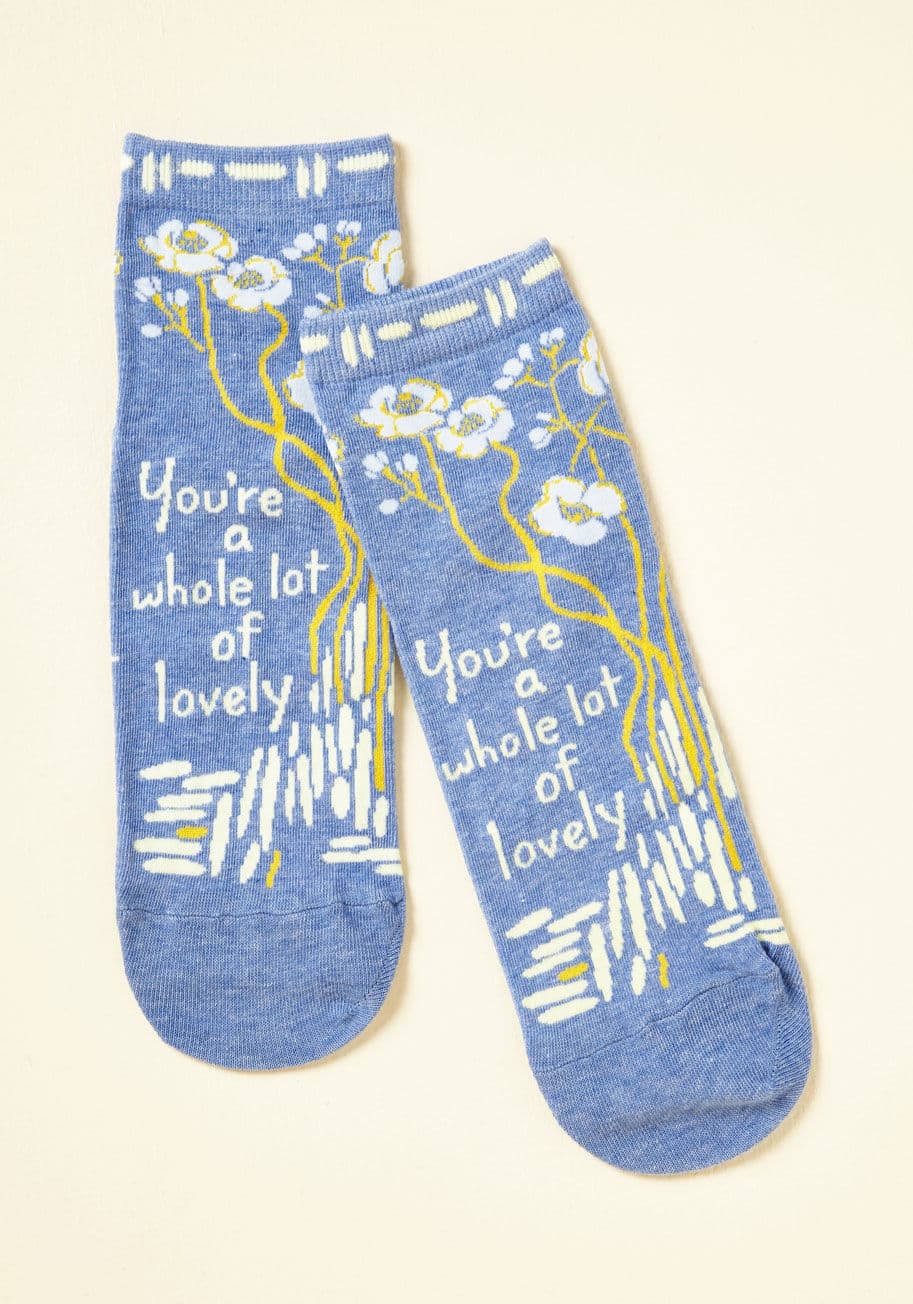 SW601 - Like any good pick-me-up, these blue socks will make you smile every time you put them on! Knit with yellow and white floral print as well as an encouraging personal truth, this pair will make you grateful you can snuggle your toes into so much positivity